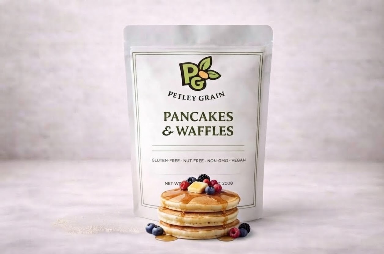 Petley Grain Pancakes & Waffles mix pouch in front of a stack of pancakes with berries and maple syrup